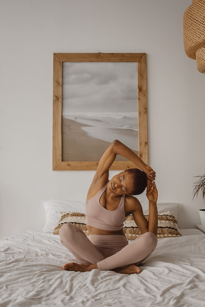 Black Women practicing Yoga in Bed. A beautiful Way to practice self-care during cycle syncing.